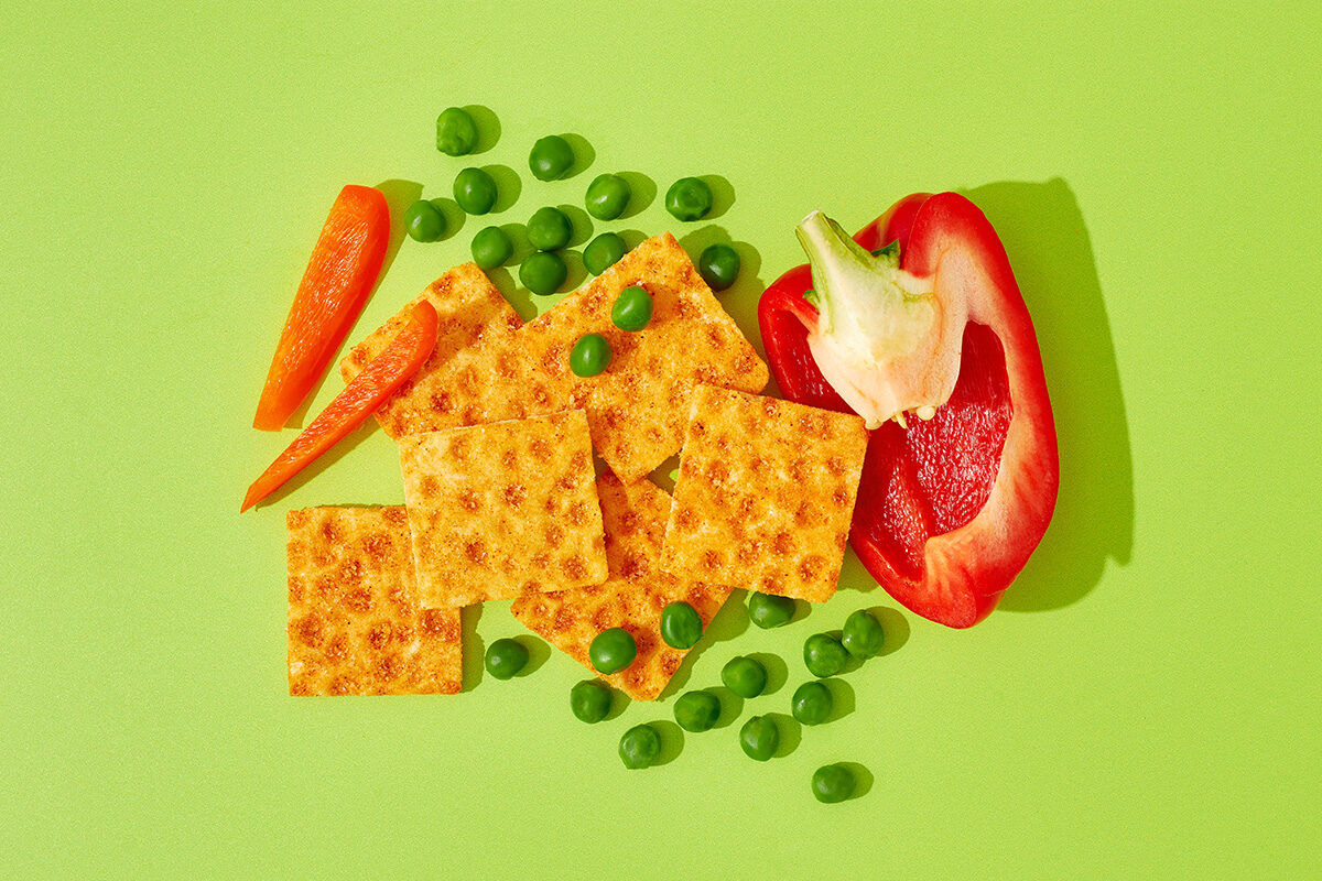 Knäckebrotsnack neben Paprika und Erbsen auf grünem Untergrund, Foodfotografie