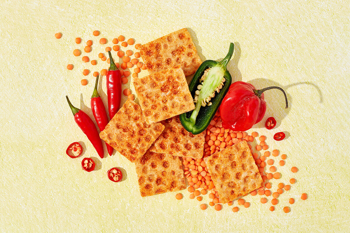 Knäckebrotsnack neben Chillischoten und Roten Linsen auf gelbem Untergrund, Foodfotografie
