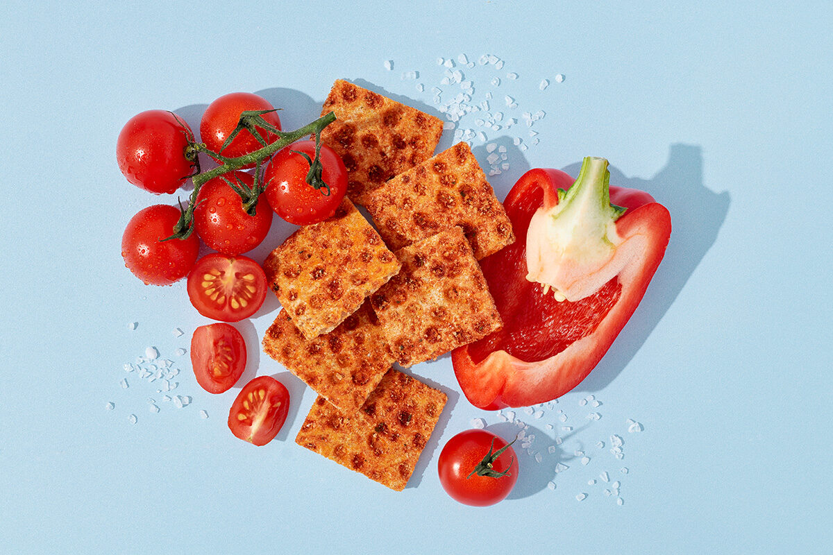 Knäckebrotsnack neben Tomaten, Paprika und Meersalz auf blauem Untergrund, Foodfotografie
