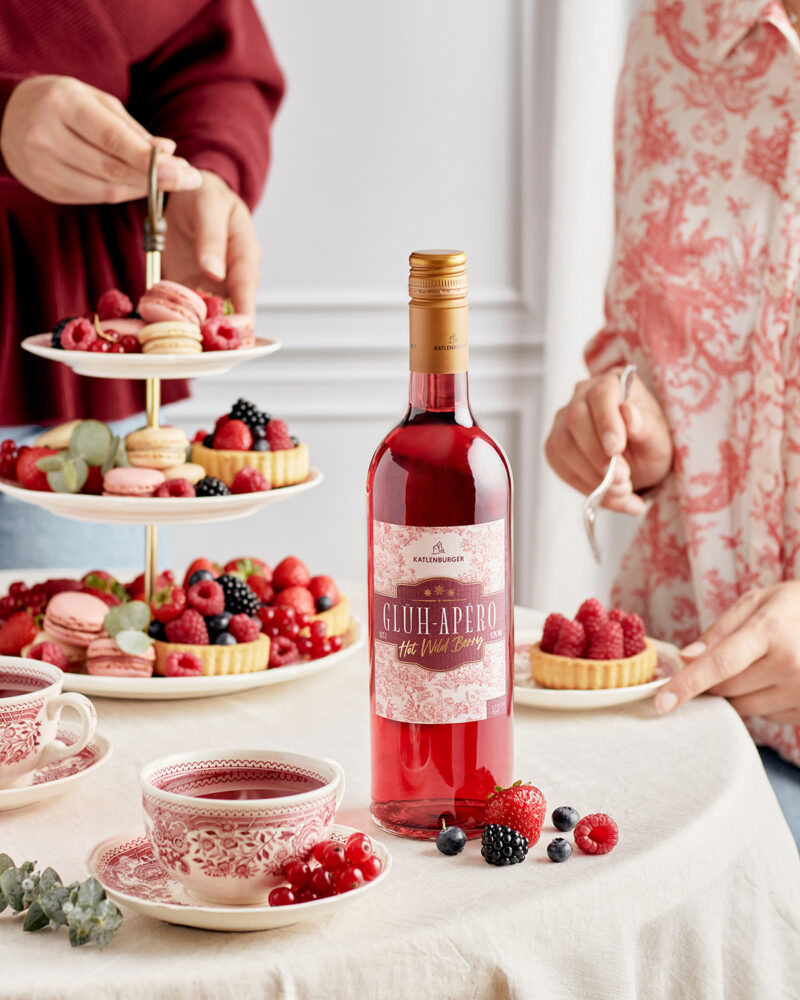 Flasche Glüh-Apero steht auf Tisch neben Etagere und Beeren, Beveragefotografie