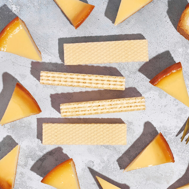 Waffelstücke und kleine Käsekuchenstücke liegen auf grauer Fläche, Foodfotografie